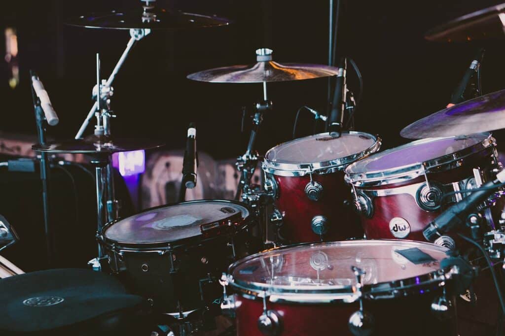 Batterie sur scène avec toms, cymbales et microphones, éclairage sombre. Logo DW visible sur une caisse.