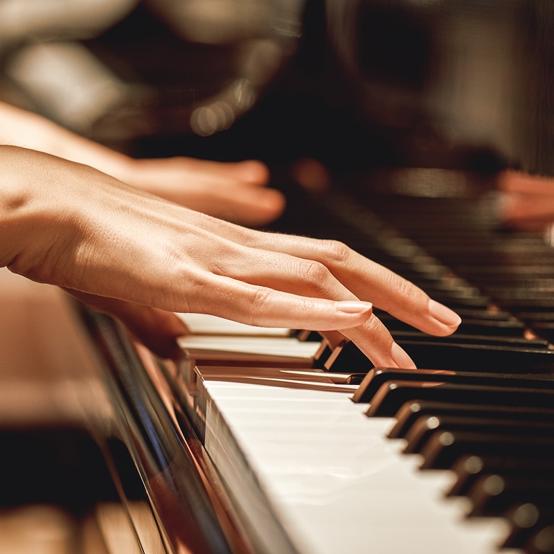 Gros plan sur des mains jouant du piano, les doigts touchant les touches noires et blanches. Ambiance musicale chaleureuse.