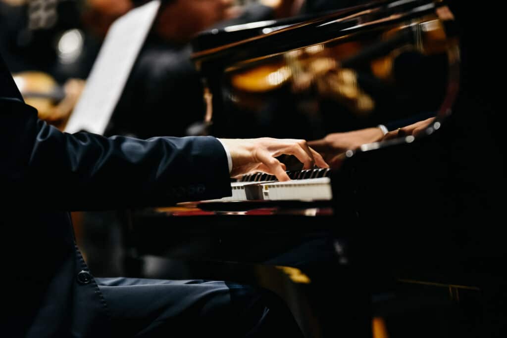 Mains d'un pianiste sur le clavier d'un piano à queue lors d'un concert. Reflet de l'orchestre sur l'instrument.
